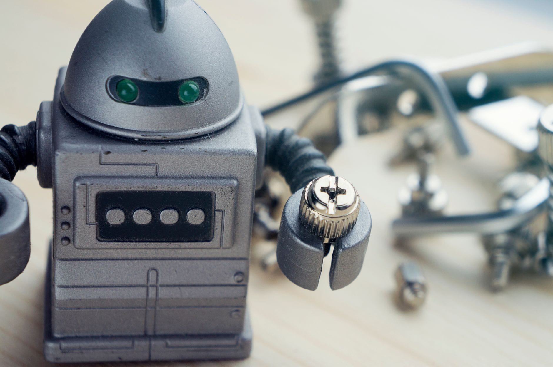 Zbliżenie zabawkowego robota z śrubą w rękach, otoczonego narzędziami