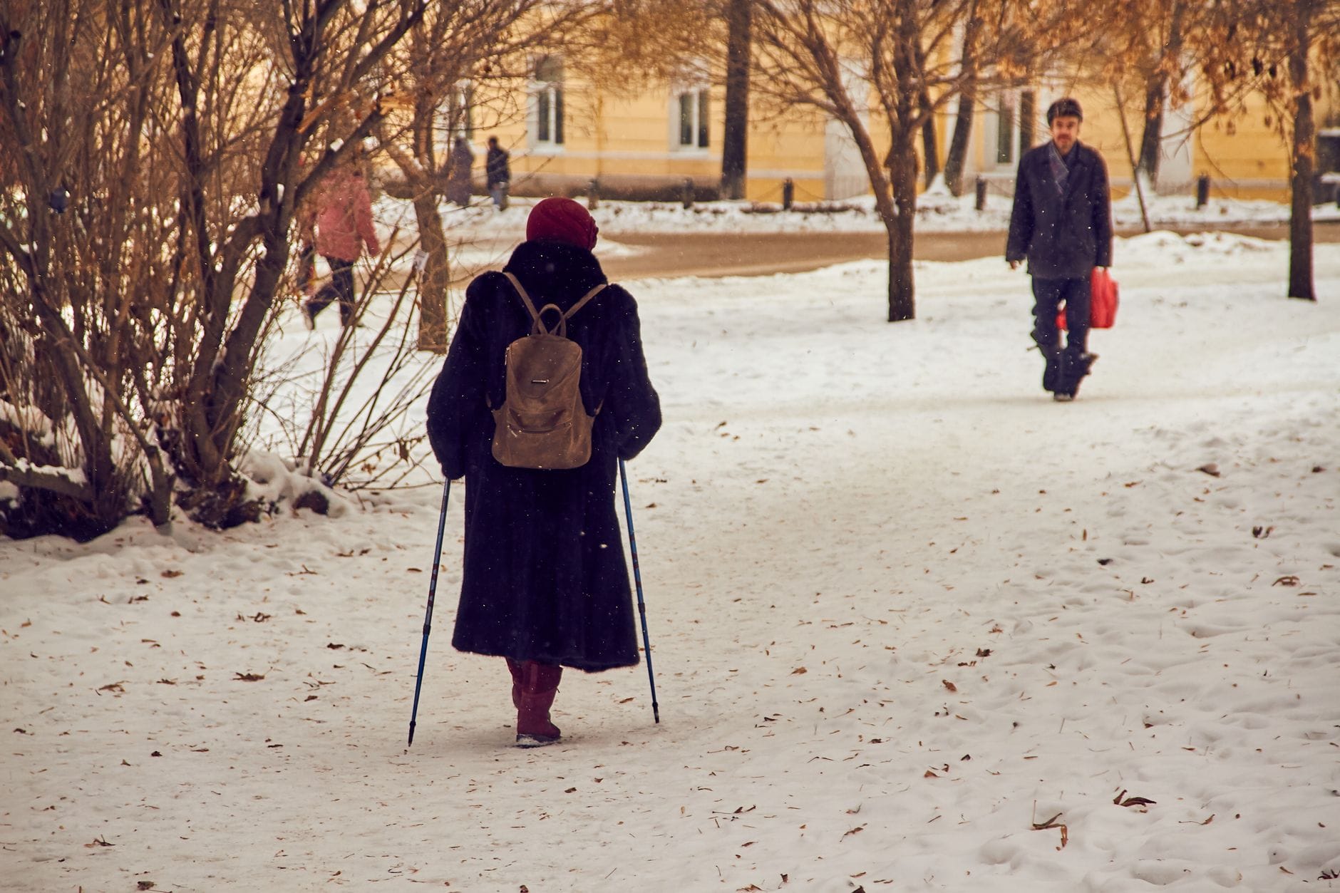 Spacerowicze w zimowych płaszczach idący przez ośnieżony park