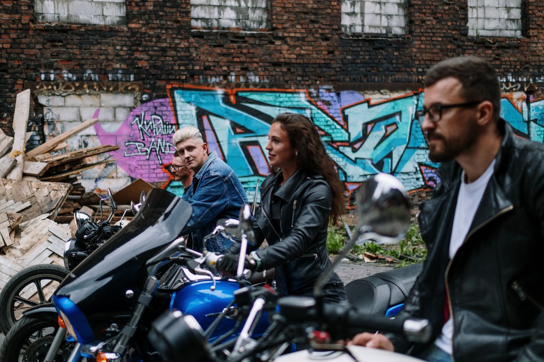 Trzech motocyklistów przy motocyklach na tle miejskiego graffiti