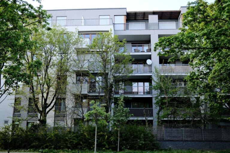 Nowoczesny blok mieszkalny otoczony zielonymi drzewami i krzewami